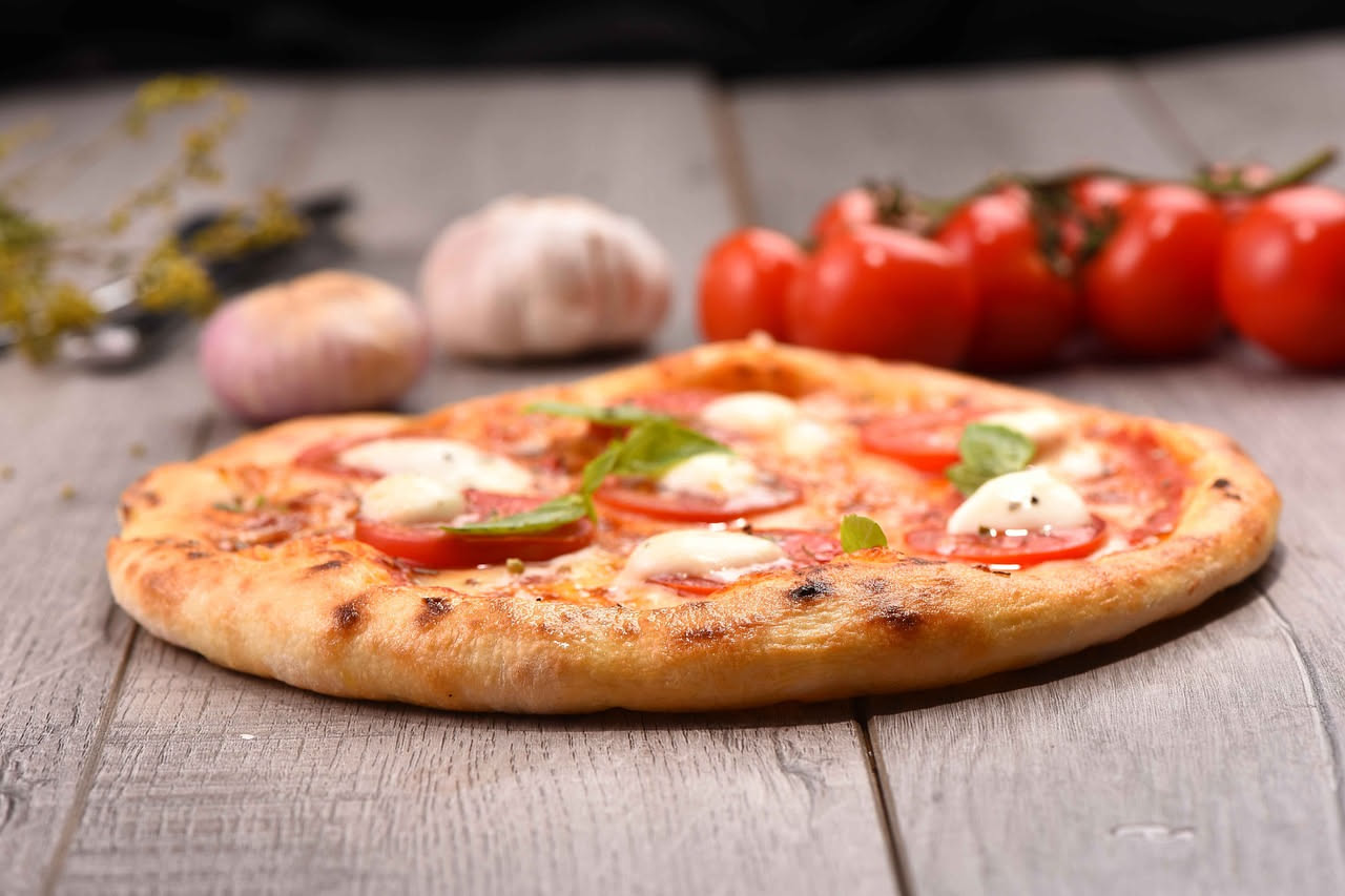 Pizza napoletana con aglio affettato sottile, origano secco verde e filo di olio extravergine su impasto dorato al forno a legna