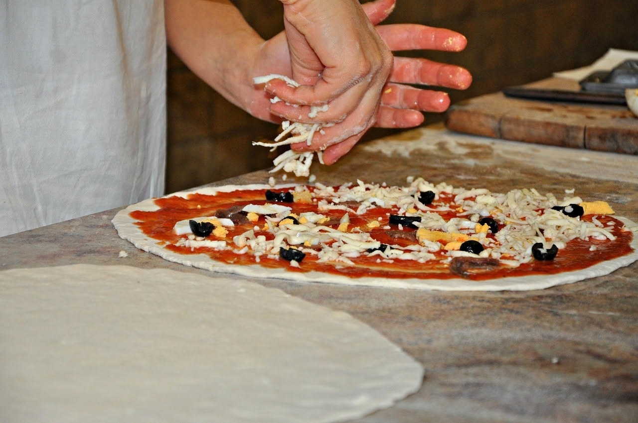 Un impasto bianco e lievitato in una ciotola di terracotta, con bolle di fermentazione visibili sulla superficie, circondato da chicchi di grano e una brocca d'acqua