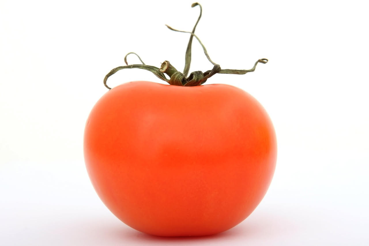 Pomodori rossi maturi appena colti con stelo verde, disposti su una superficie di legno rustico accanto a una foglia di basilico fresco