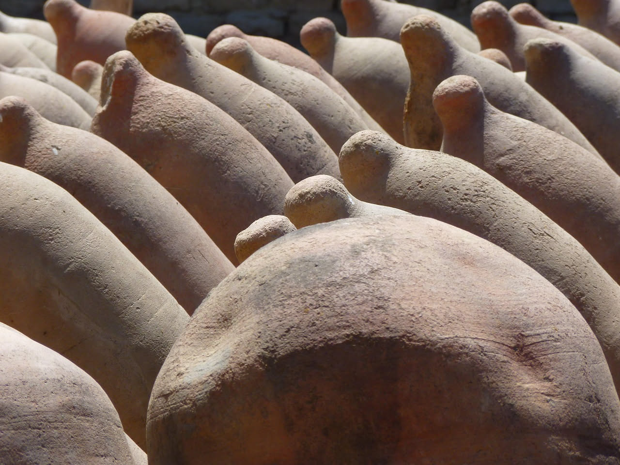 Un testo di terracotta grezzo, tondo e piatto, poggiato su una pala di legno davanti a un forno a legna tradizionale con fiamme rosse di fondo