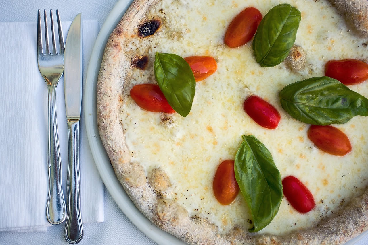 Primo piano di una pizza appena sfornata con mozzarella che forma una patina lucida e umida sulla superficie, base della pizza visibilmente bagnata ai bordi