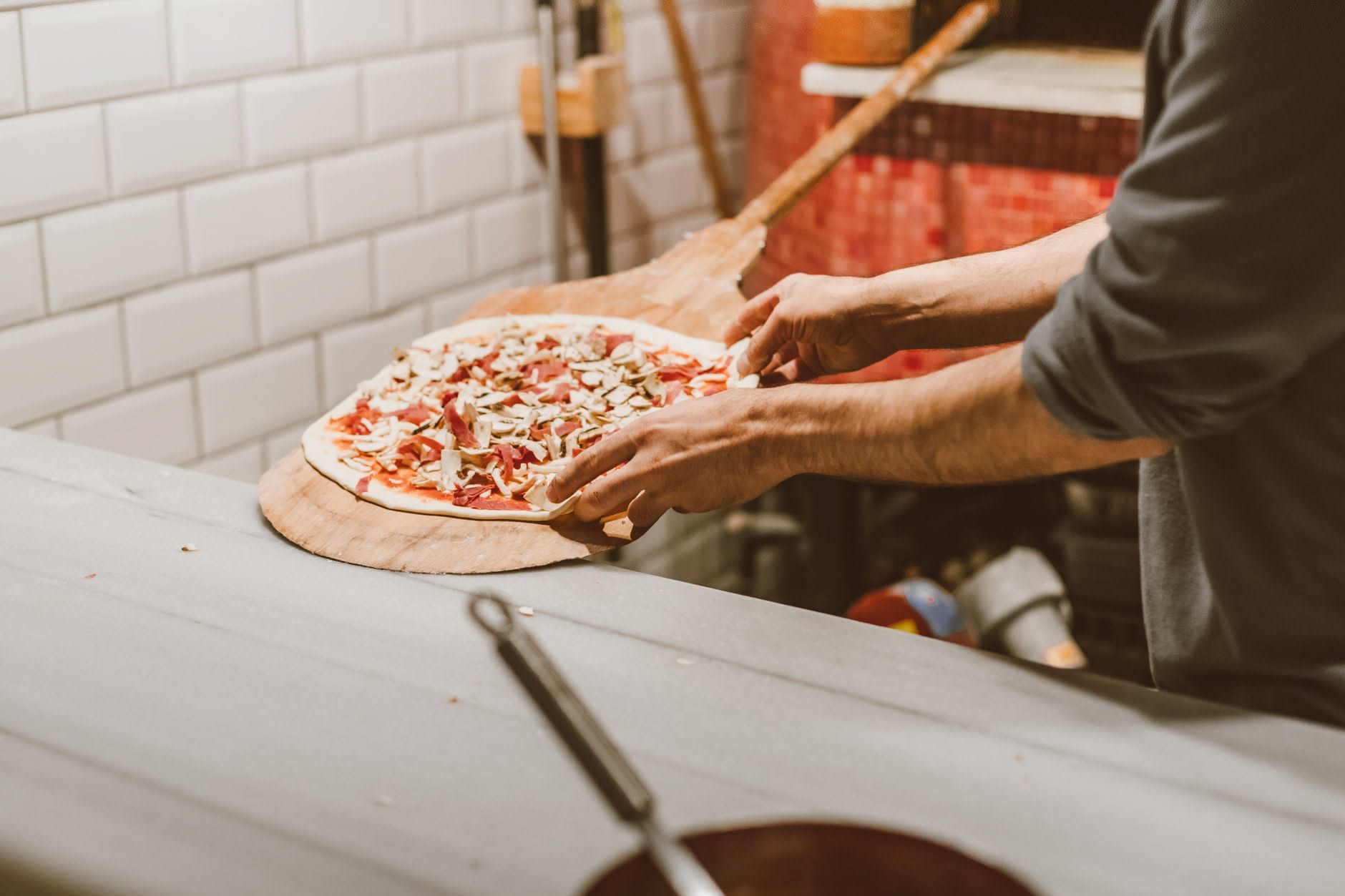 Impasto di pizza in una ciotola di ceramica bianca con cristalli di zucchero sparsi, accanto a un cucchiaio di legno e una bustina di lievito secco su un piano di lavoro in marmo