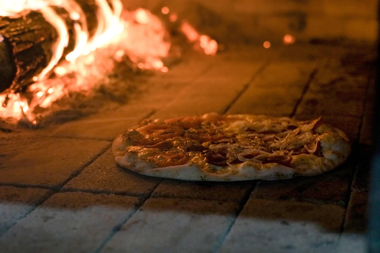 Pizzaiolo napoletano che lavora l'impasto con le mani nude sopra un bancone di legno, con il forno a legna sullo sfondo che irradia calore rosso arancio