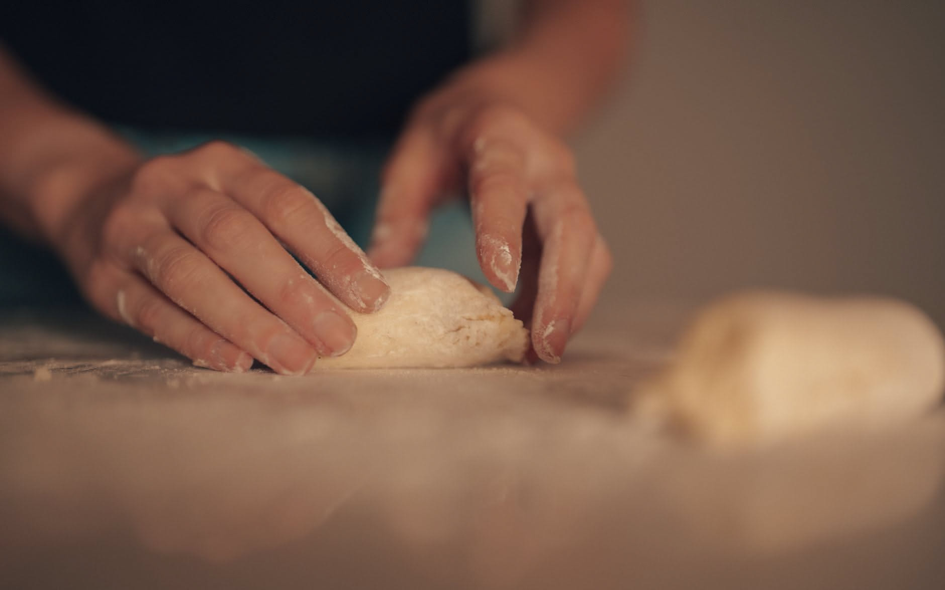 Mani di un pizzaiolo che allargano un disco di impasto su un tavolo infarinato, con l'impasto che tira leggermente verso il centro