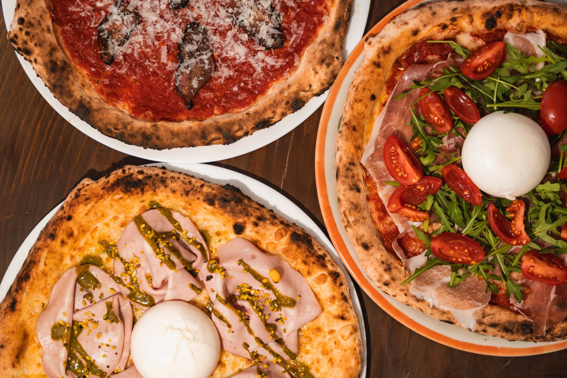 Pizza napoletana appena sfornata con cornicione gonfio e morbido, confrontata con impasto steso su piano di lavoro in cucina domestica