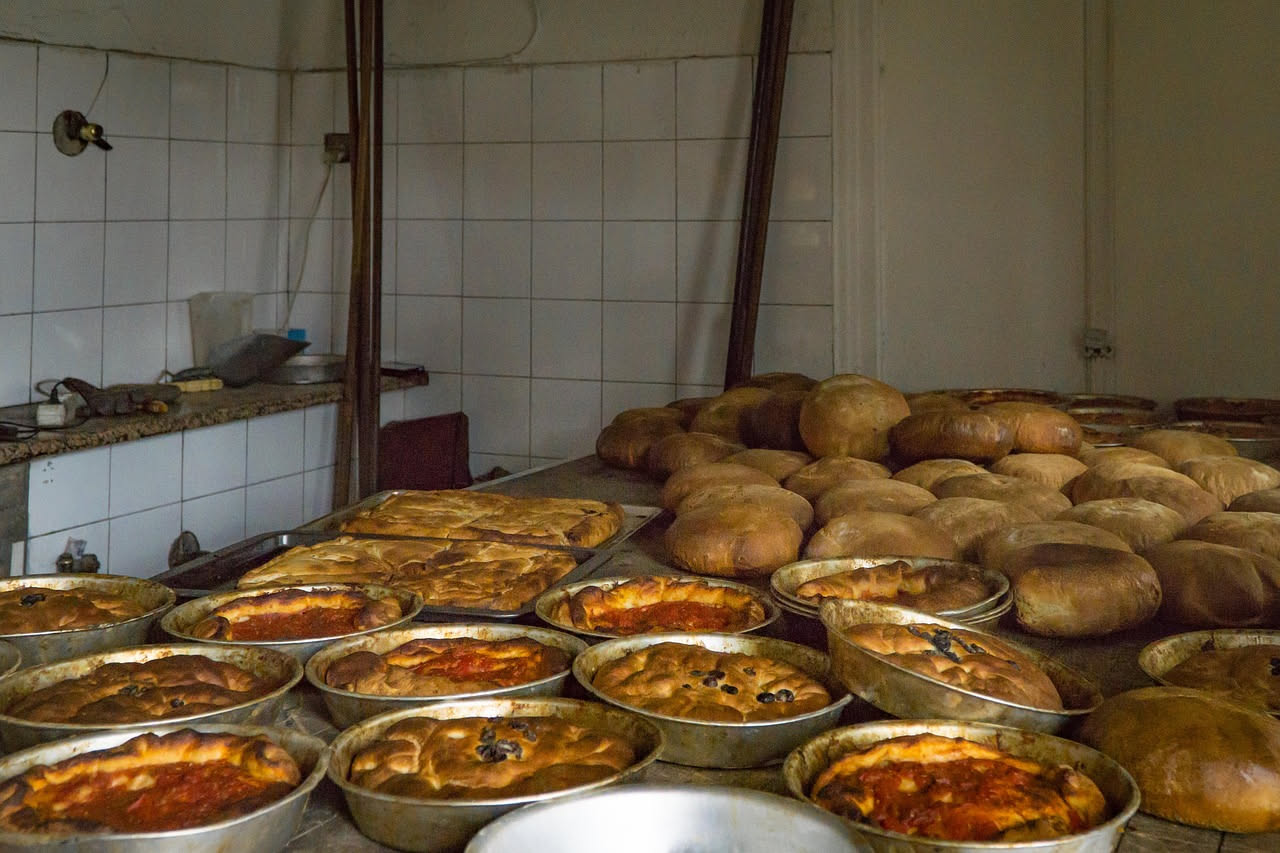 Pane rustico scuro appena sfornato con crosta dorata, tela di lino bianca e mattone di forno antico sullo sfondo, stile Settecento
