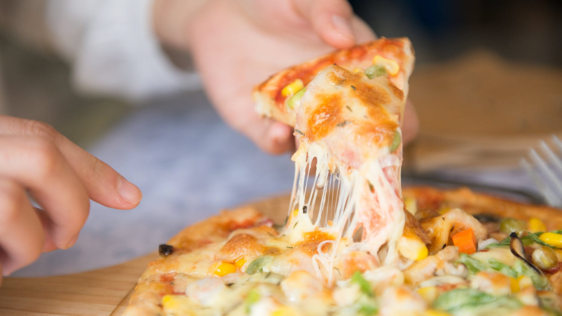 Fetta di pizza con mozzarella e pomodoro che cuoce in una padella antiaderente su fiamma media, con coperchio trasparente a metà copertura