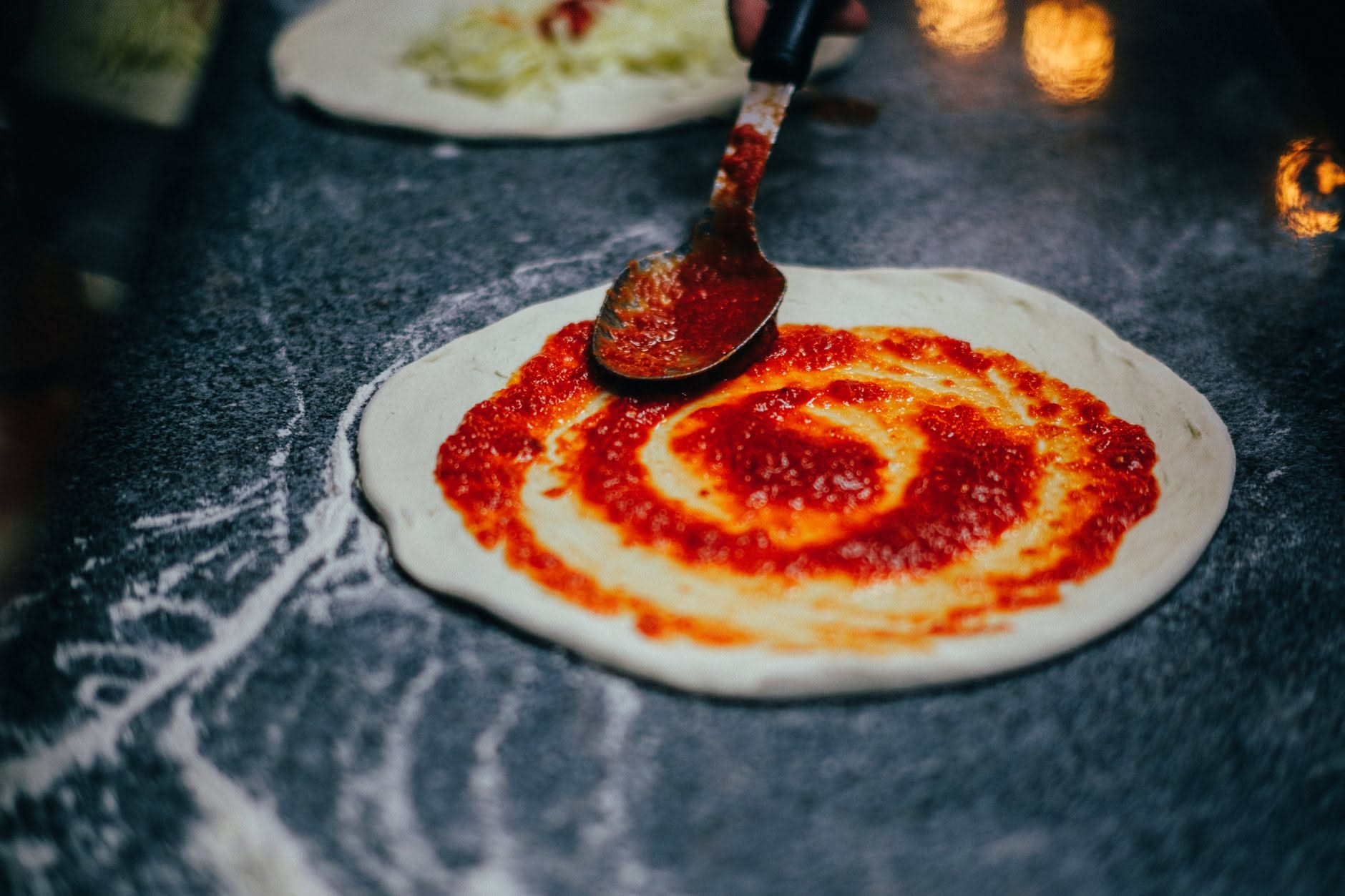 Disco di impasto steso con salsa di pomodoro distribuita a spirale e mozzarella appoggiata sopra, prima della cottura
