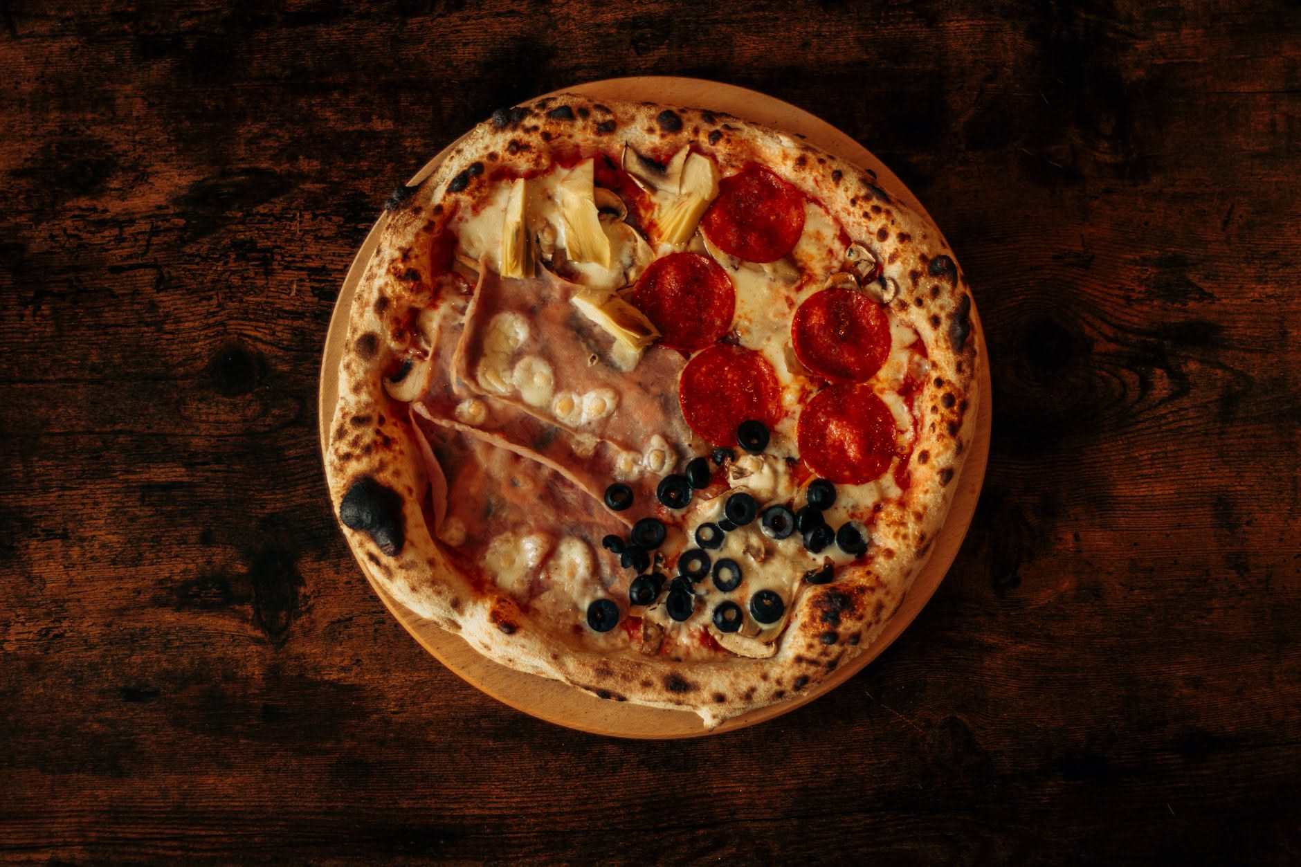 Pizza quattro stagioni divisa in quattro spicchi con carciofi, funghi, prosciutto e olive